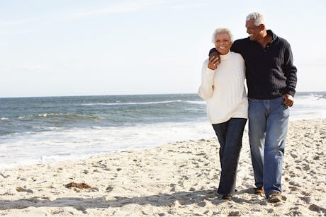 Mature couple walking on the beach discusing cancer prevention